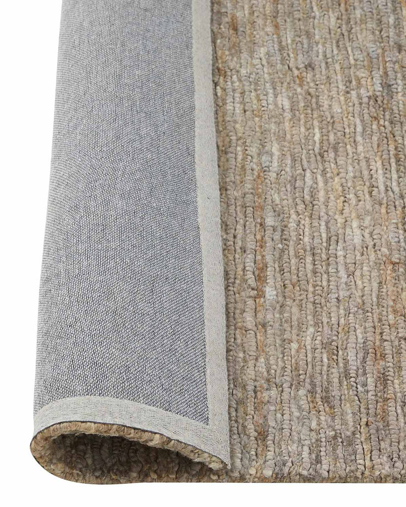 A textured jute floor rug in soft beige with the corner flipped up to show the durable cotton backing. 