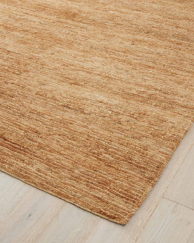 A corner image of a natural warm brown floor rug made with textural jute fibres in a cut loop stitch. 