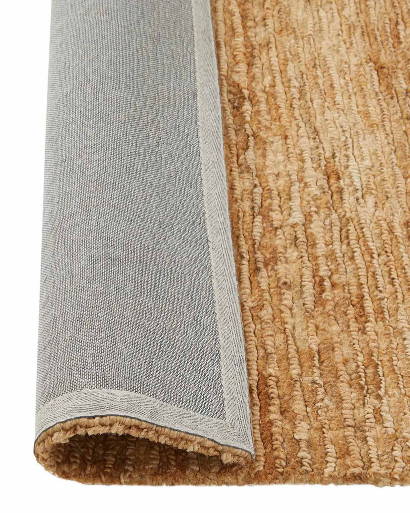 A corner image of a cut and loop pile textured brown floor rug in 100% natural jute with the edge flipped to show the durable cotton backing. 