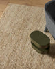 A chair and designer end table on top of a natural warm cream toned jute floor rug. 