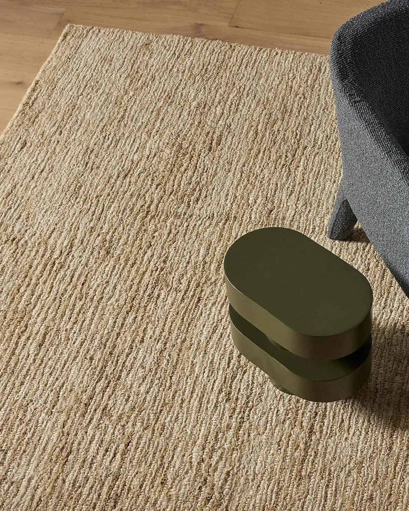 A chair and designer end table on top of a natural warm cream toned jute floor rug. 