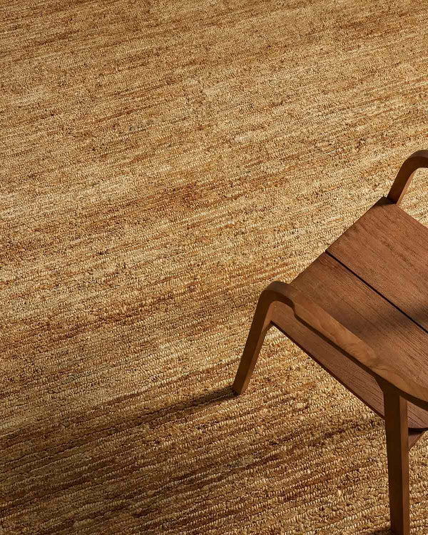 A modern chair sitting atop a natural jute floor rug with textural elements in a warm brown tone. 