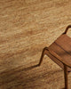 A modern chair sitting atop a natural jute floor rug with textural elements in a warm brown tone. 