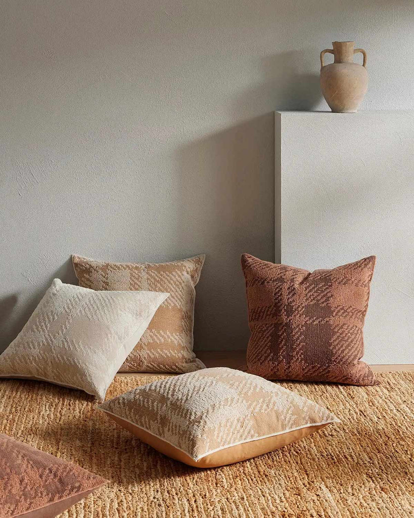 A number of pillows by Weave Home sitting atop a natural textured jute floor rug in a warm yellow brown. 