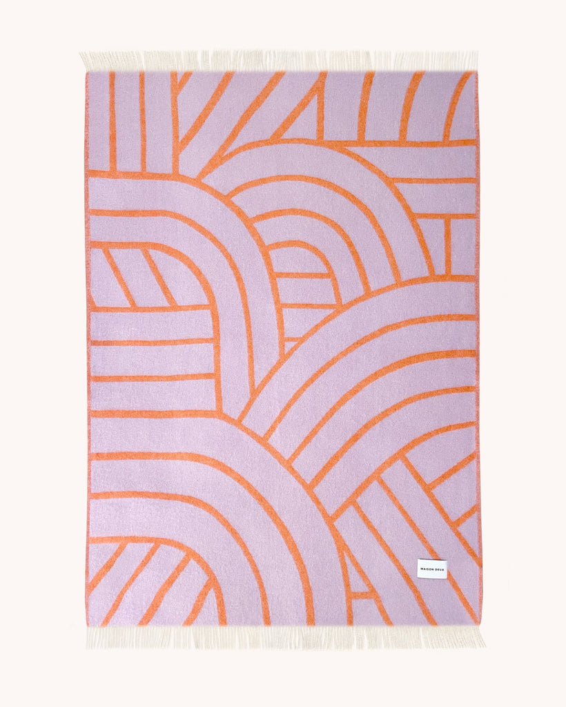 A full view of the front side of the Maison Deux NZ wool throw blanket with a lined pattern, in shades of mostly lilac with bright orange detailing.