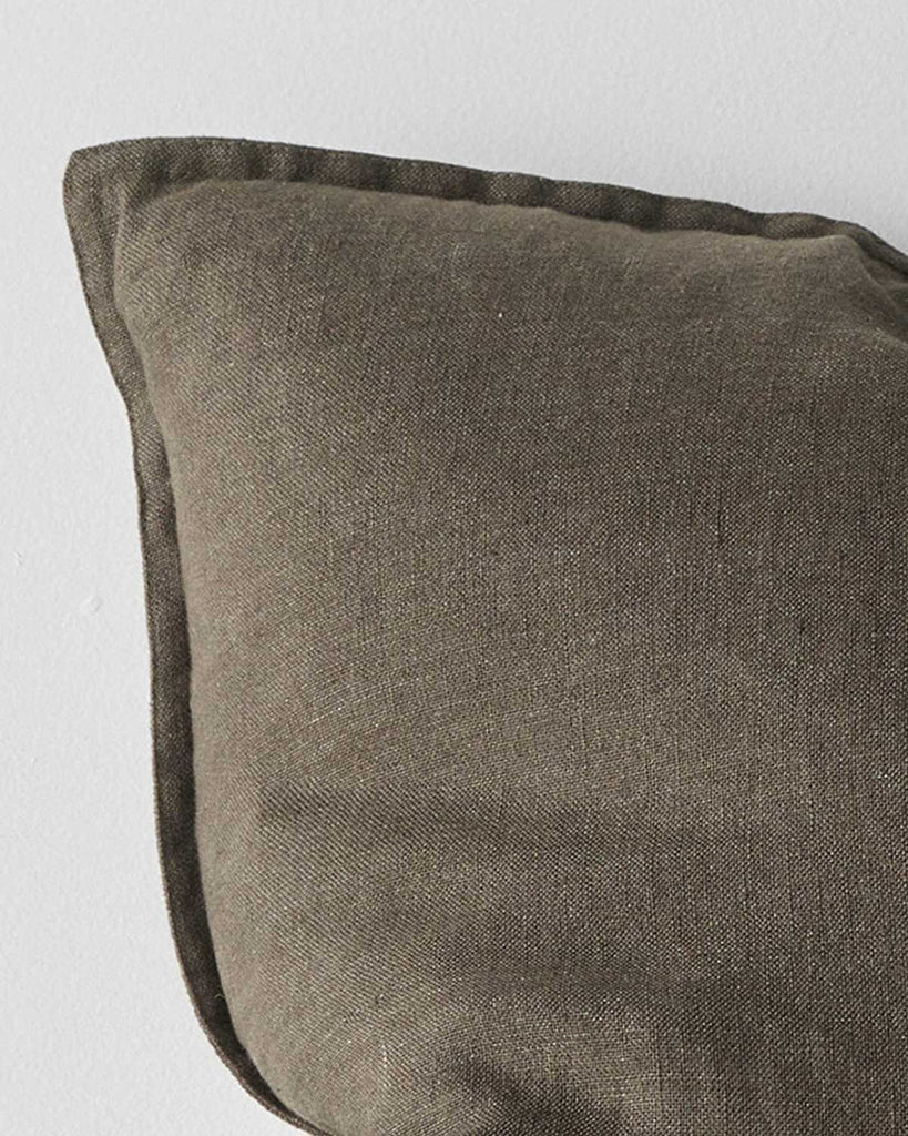 A corner of a deep warm olive green toned cushion in European linen with a flanged edge. 