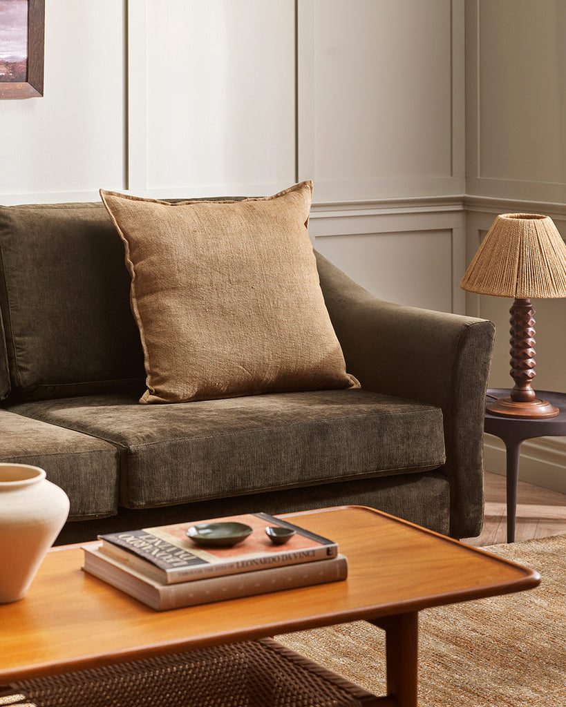 A soft yellow brown toned cushion in textured linen, in a stylish living room in earth tones. 
