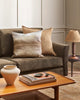 A sandy brown toned cushion next to a handpainted abstract landscape printed cushion, in an earth toned living room by Baya. 