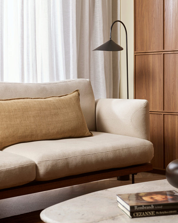 A cream toned couch in a warm living room with a yellow brown long lumbar cushion in a textural linen with a small flange. By Baya. 