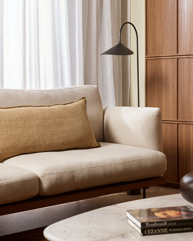 A cream toned couch in a warm living room with a yellow brown long lumbar cushion in a textural linen with a small flange. By Baya. 