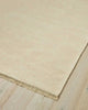 A corner of a 100% linen fibre floor rug in a soft warm cream tone with a matching fringed edge. 