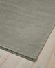 The edge of a blue grey floor rug made from 100% linen fibres with a matching fringed edge. 
