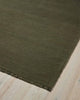 A corner image of a deep olive green floor rug with matching toned fringed edges in 100% linen. 