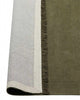 A corner image of a dark green floor rug in 100% linen, with the edge flipped up to show the durable cotton backing and the underside of the fringe edging. 