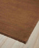 A corner image of a warm toffee brown floor rug handmade with 100% linen fibres. 