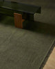 A handwoven linen fibre floor rug in olive green with fringed edges, with a modern style coffee table sitting on it. 