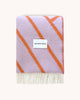 A folded, line patterned throw blanket in shades of lilac and vibrant orange, by Maison Deux