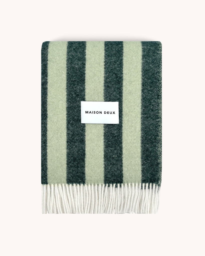A folded woolen throw blanket with a striped pattern, alternating dark and light green, by Maison Deux