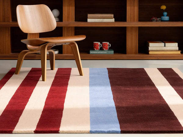The Marimekko Ralli wool floor rug in striking red, maroon, cream and blue stripes, seen in a modern home