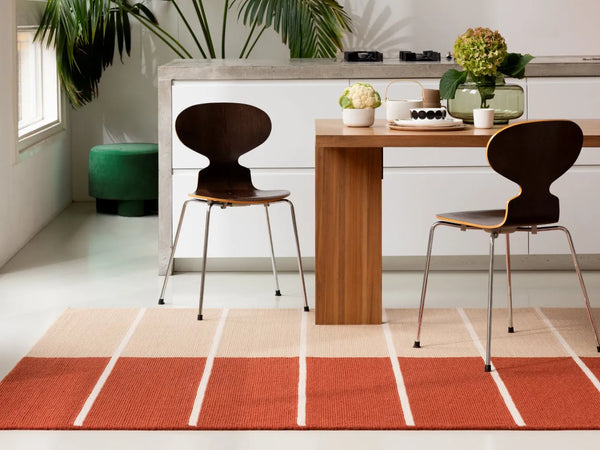 The Marimekko Tiibet floor rug, made from recycled PeT yarns, in burnt orange colour, seen under a dining table