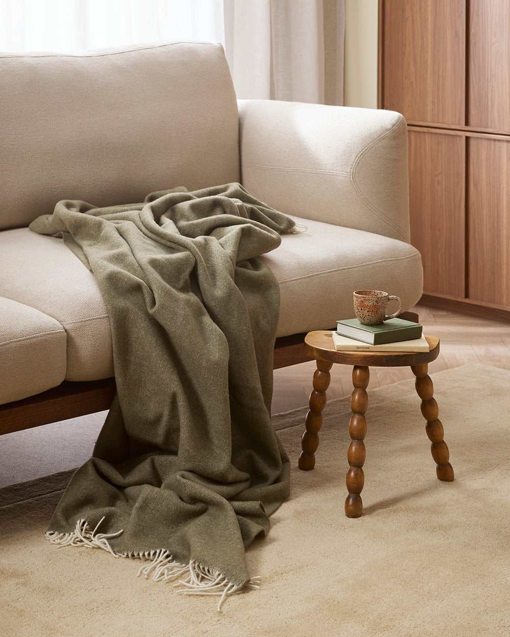 A soft olive green merino wool throw blanket draped over a cream coloured couch.