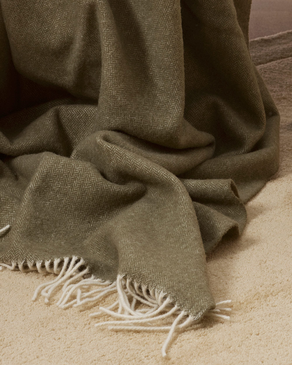 A detailed view of the cream twisted edging of an olive green merino wool throw blanket. 