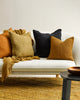 The black Baya flaxmill linen cushion on a couch with some brown and orange cushions