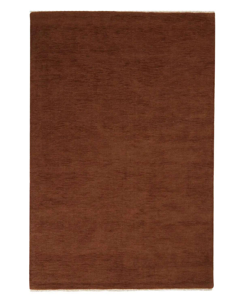A full image of a red brown earthy wool floor rug with subtle cream coloured fringe edging. 