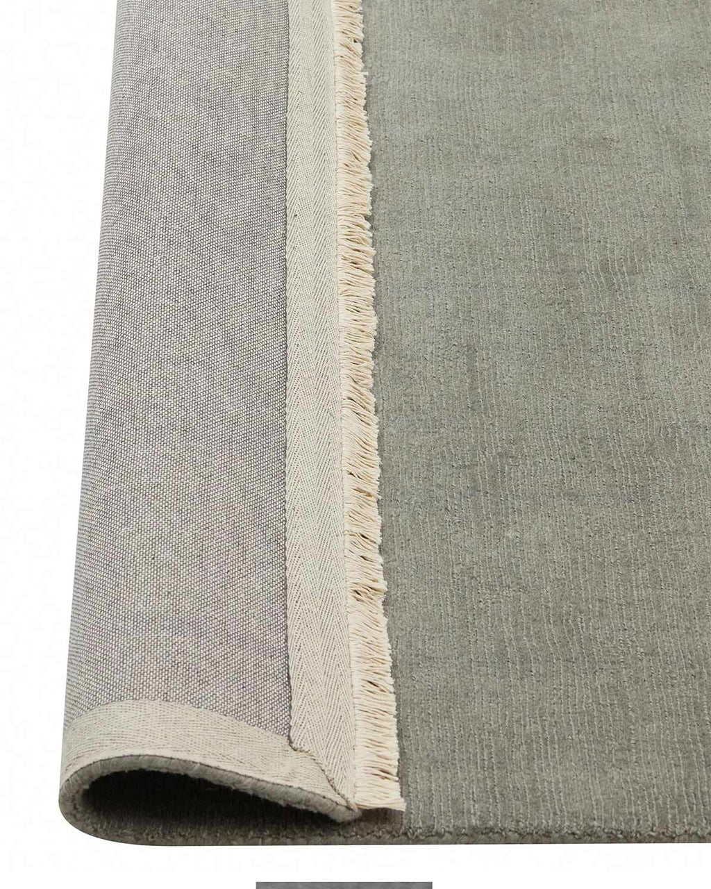 A grey green 100% wool floor rug with cream fringe edges, the corner of which is flipped up to show the cotton backing. 