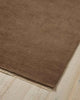 A corner image of a cool beige brown floor rug in 100% wool with slight linear texture in the weave and a cream fringed edge. 