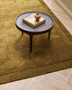 A coffee table on top of a luxurious warm green toned floor rug in 100% NZ wool with cut pile frame detailing along the edges, by Baya. 