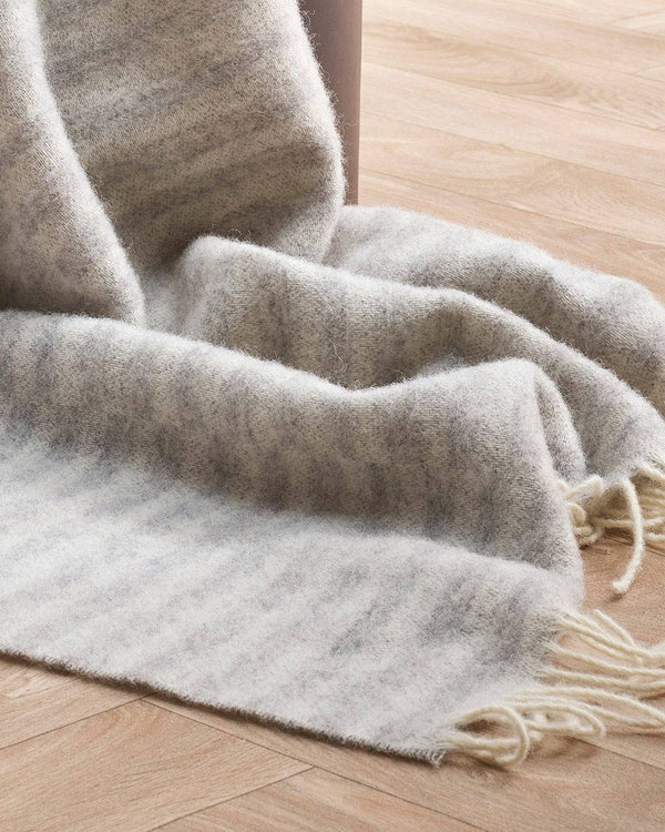 A detailed view of the striped Noah blanket in neutral silver with cream twisted edgings, in 100% wool. 