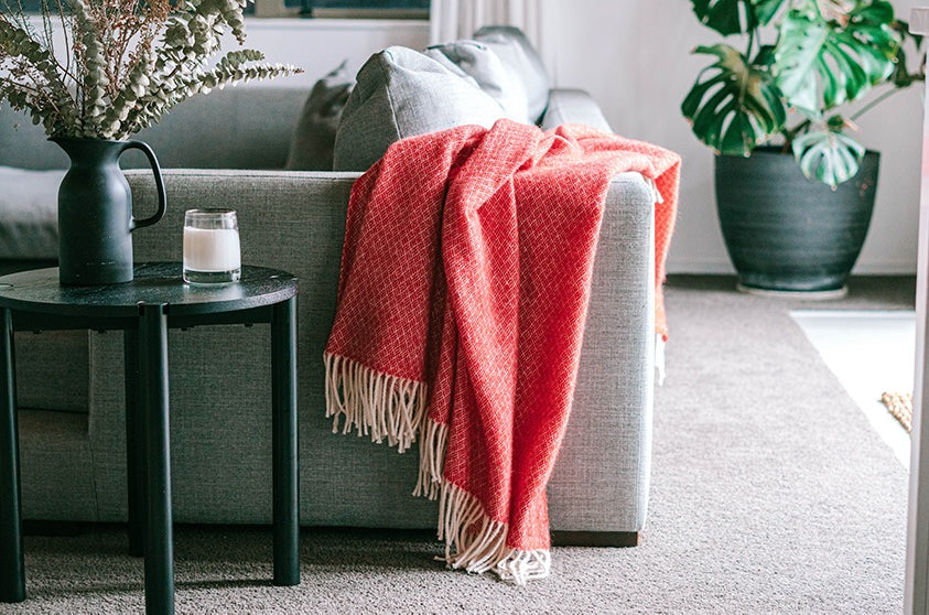 100% wool NZ throw blanket by Ruanui Station, in vibrant 'Rakaia red', shown draped over a couch