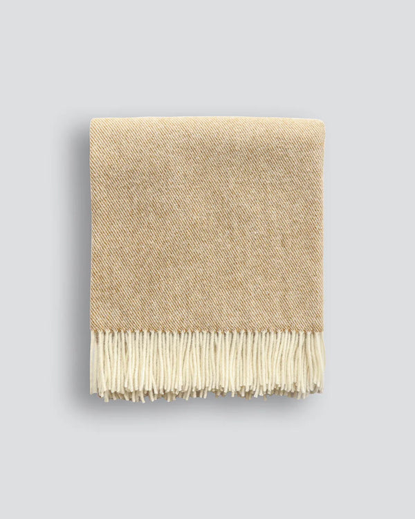 A beautiful NZ made throw blanket in 100% NZ wool, featuring a twill weave and trending ochre colour, shown folded with twisted fringe