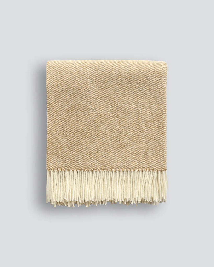 A beautiful NZ made throw blanket in 100% NZ wool, featuring a twill weave and trending ochre colour, shown folded with twisted fringe