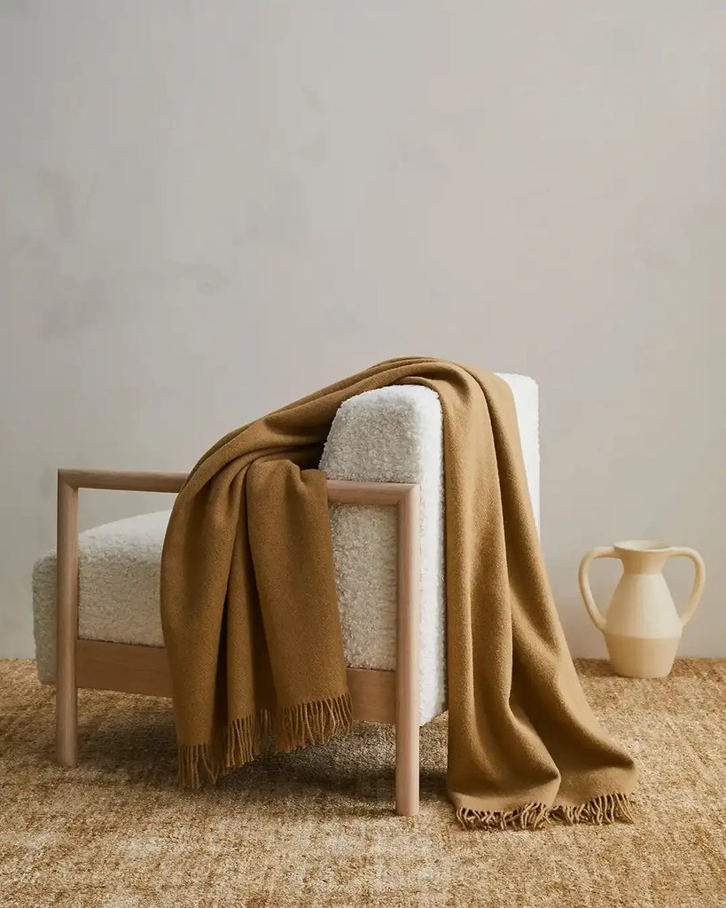 Weave Home wool throw blanket in colour 'camel' - a light brown, draped over a chair