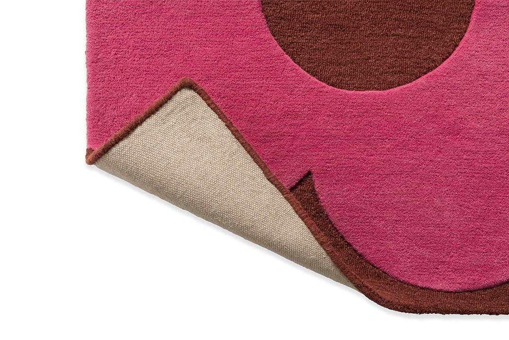 The Orla Kiely Sprig Stem floor rug in colour 'paprika' pink and red, seen with the corner lifted to reveal underneath