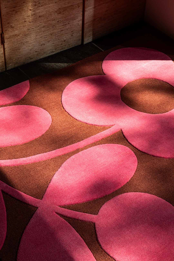 The Orla Kiely Sprig Stem floor rug in colour 'paprika' pink and red, seen close up in sun and dappled light