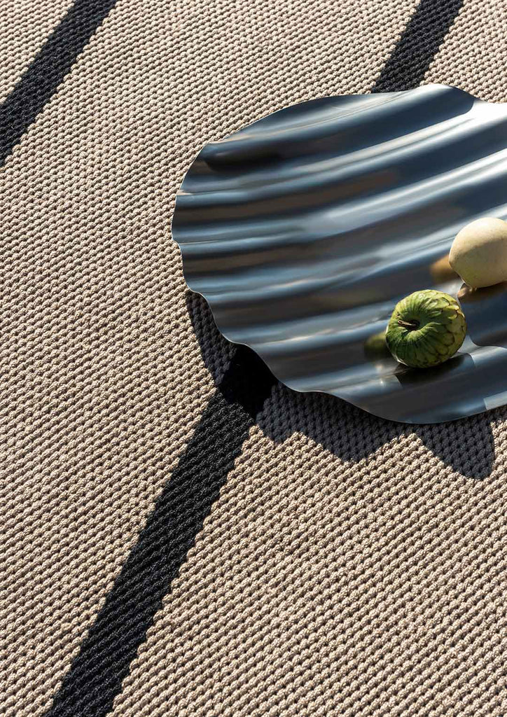Close up of a premium summer outdoor rug by Brink and Campman, featuring a charocal-black and beige stripe design