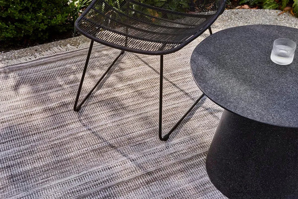 Sand coloured neutral outdoor rug by Globe West and Soren Liv, seen outdoors under a tabel and chair