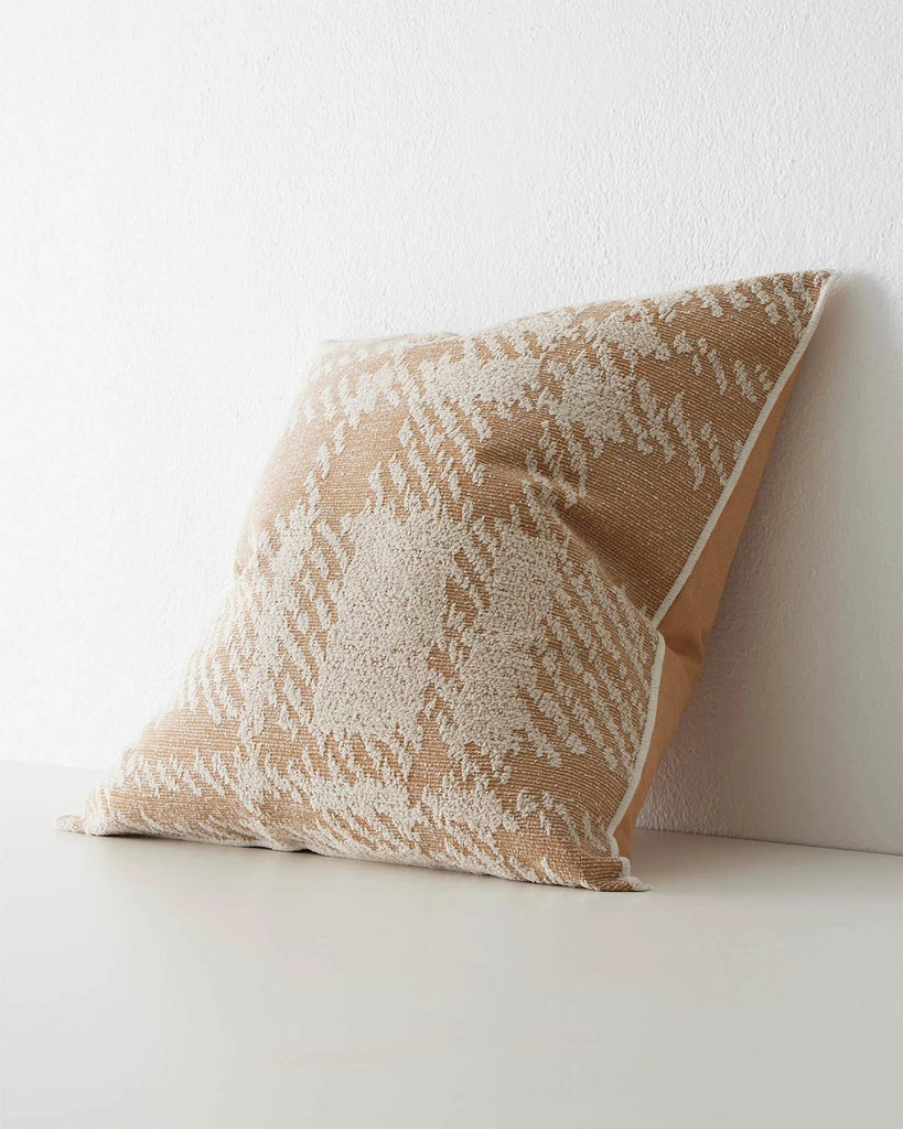A side view of a patterned cushion with an oversized check print, in shades of muted orange and white. 