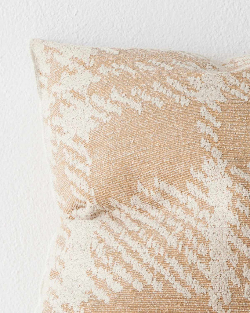 A close up image of a textural check patterned cushion in shades of light orange and off-white. 