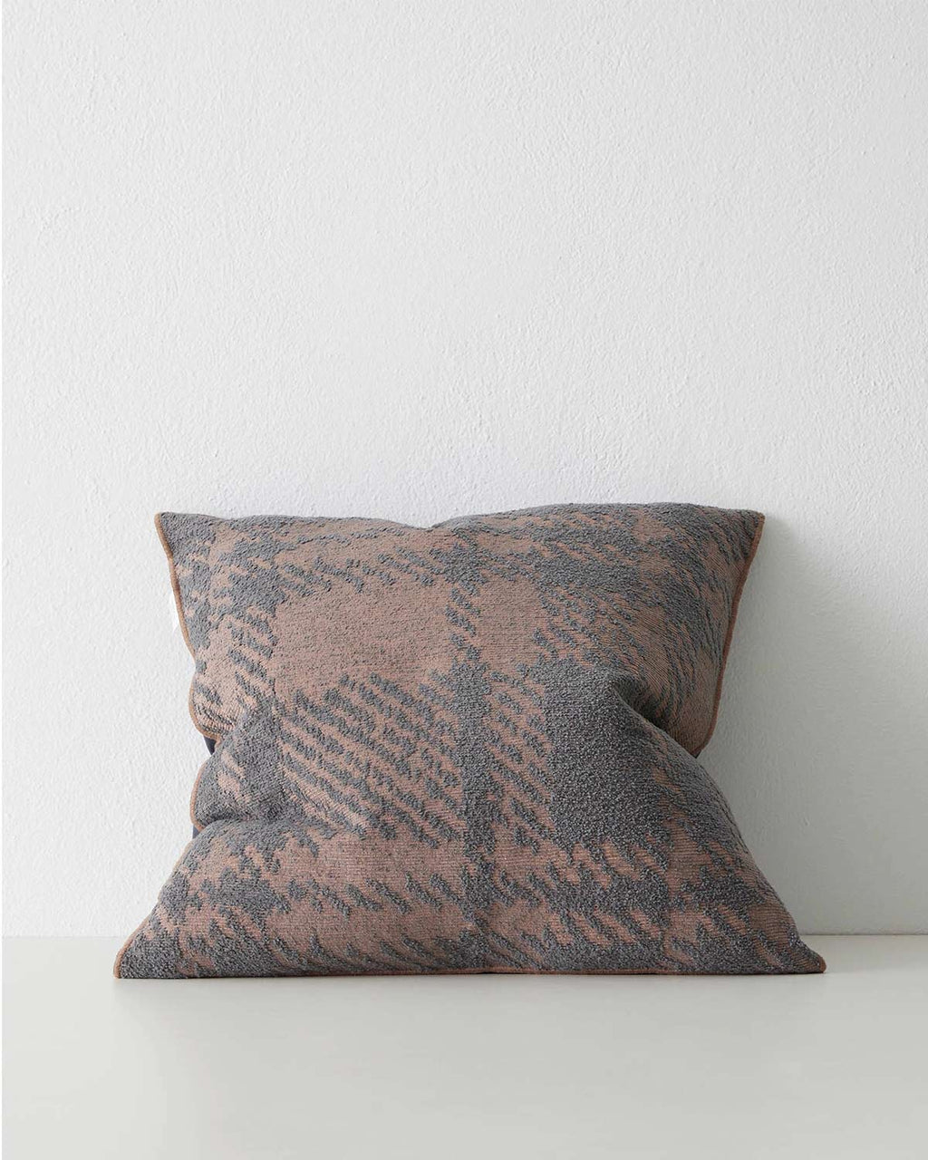 A textural cushion with an oversized check pattern in muted shades of dusky rose and deep purple 