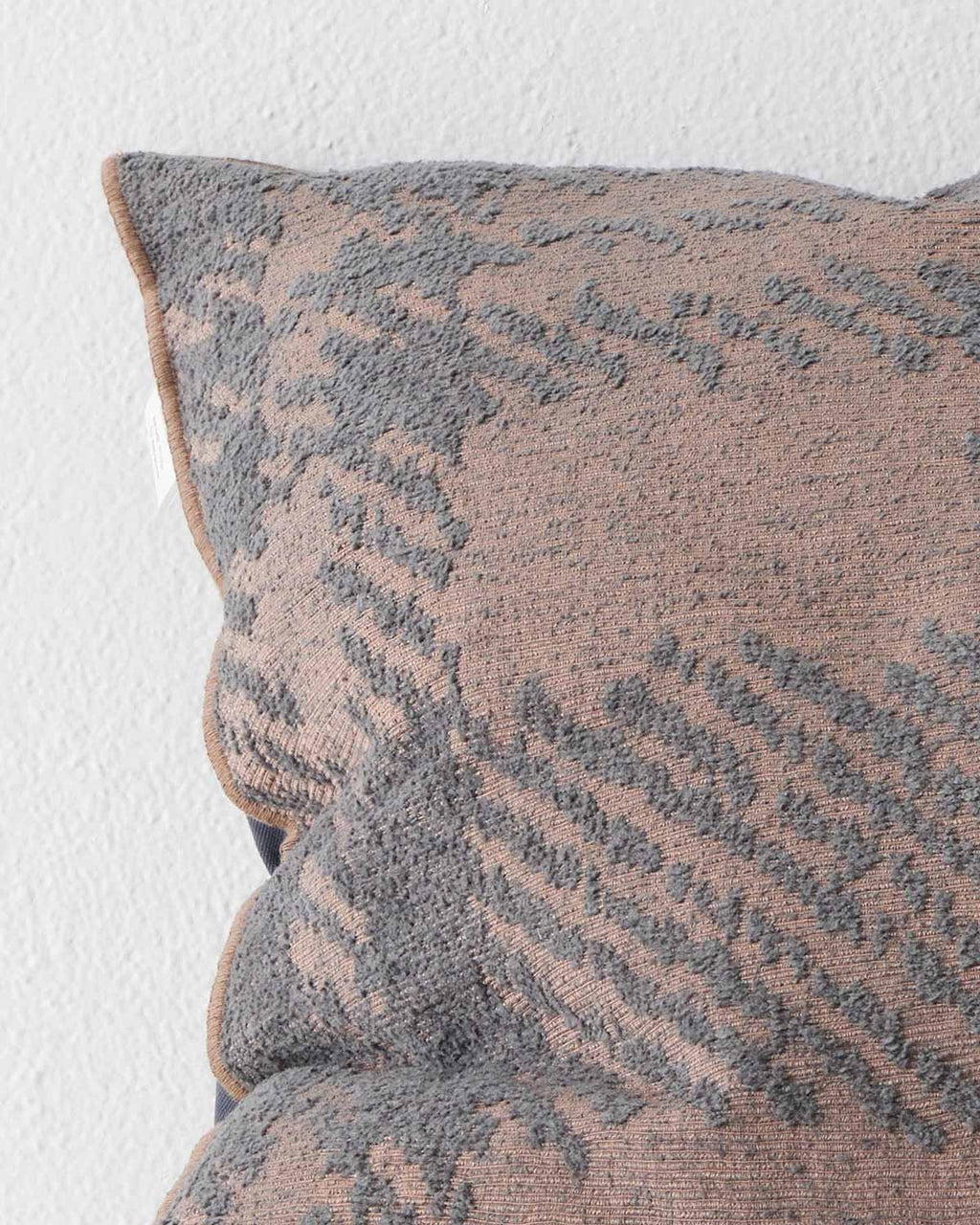 A close up image of a textural check patterned cushion in muted pink and purple tones. 