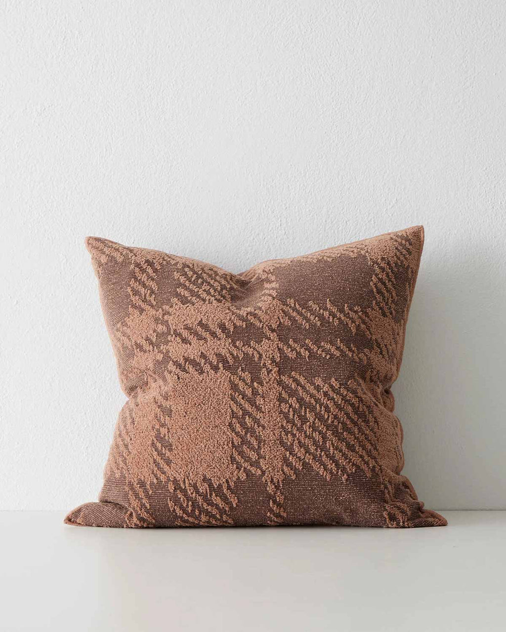 A textural cushion with an oversize check pattern in shades of rust orange and deep sienna red brown. 