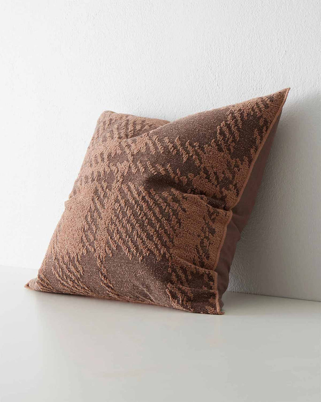 A side view of a patterned cushion in red brown clay tones. 