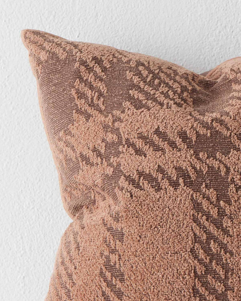 A detailed view of a textural patterned cushion in tones of muted orange and brown. 