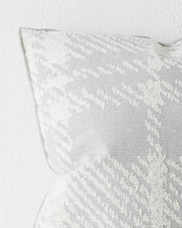 A close up view of a cushion with a textured check pattern in blue-grey and white. 