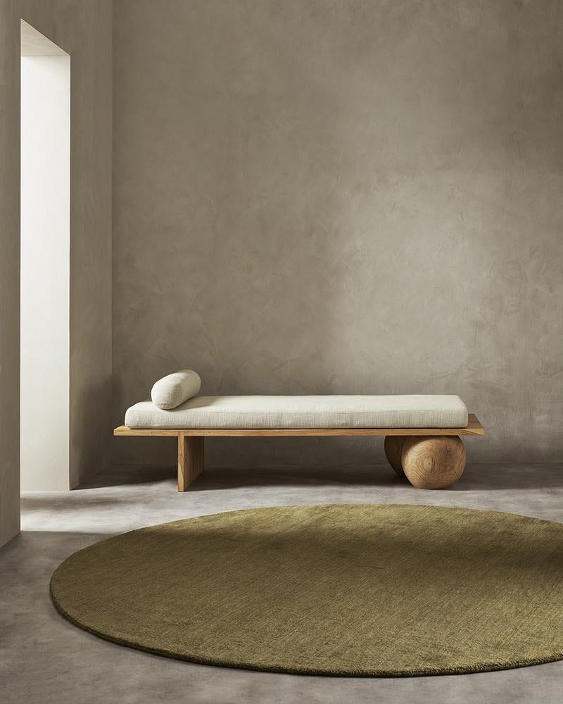 A minimalist sitting area with a modern style couch and a round green floor rug in 100% wool fibres. 