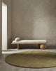 A minimalist sitting area with a modern style couch and a round green floor rug in 100% wool fibres. 